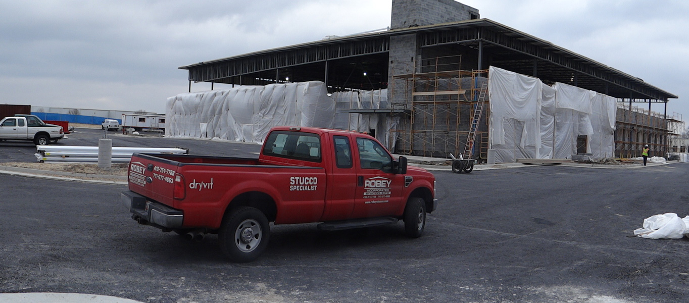 red Robey Stucco Specialist truck parked in front of a building under construction